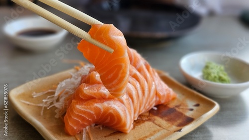 Chopsticks holding salmon sashimi. Salmon Sashimi and wasabi on disc.