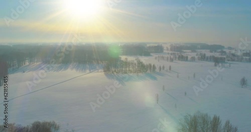 Drone aerial view of cold winter landscape arctic field, trees covered with frost snow, ice river and sun rays over horizon. Extreme low temperature weather.