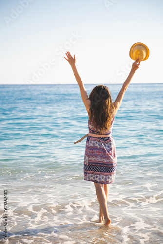 Canvas Print a girl in summer in a dress and hat on the ocean shore with her feet in the sea