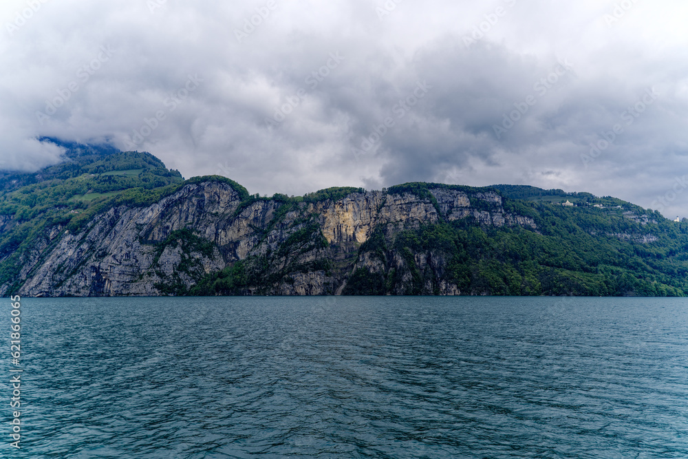 Scenic landscape with cliff and woodland at lakeshore of Lake Lucerne seen from passenger ship on Lake Lucerne on a cloudy spring day. Photo taken May 18t, 2023, Treib, Canton Uri, Switzerland.

