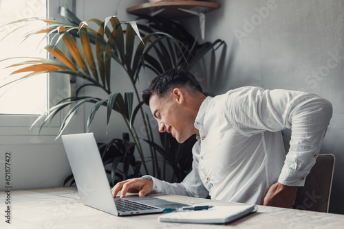 Fotografija Unhappy Caucasian man sit at desk in home office work on laptop suffer from lower back muscle strain or spasm