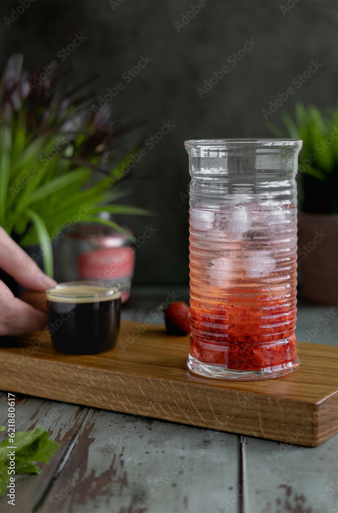 A glass with tonic, crushed strawberries and ice and a hand holding a glass ladle with coffee. Cooking a summer refreshing drink - tonic espresso.
A glass with tonic, crushed strawberries and ice and a hand holding a glass ladle with coffee. Cooking a summer refreshing drink - tonic espresso.