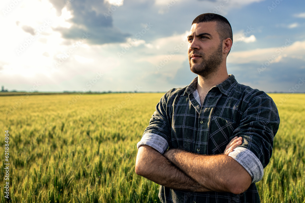 Portrait of young farmer standing in a green wheat field at sunset.