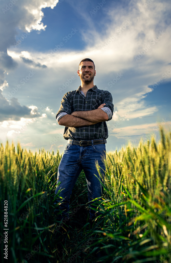 Portrait of young farmer standing in a green wheat field at sunset. Portrait of young farmer standing in a green wheat field at sunset.