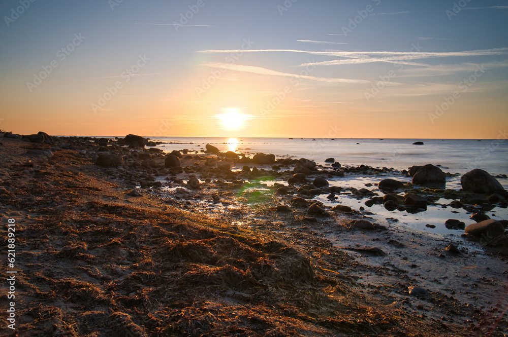 Sunset, stone beach with small and large rocks in front of the illuminated sea.