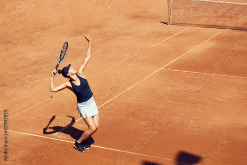 Top view image of professional tennis player in motion, young woman serving ball with racket, training at open air stadium, court. Concept of sport, hobby, active lifestyle, health, strength, ad © master1305