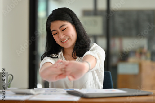 Portrait image of Young Asian businesswoman or female office worker stretching her arms during working, Break time during work, Self-stretching to reduce the incidence of office syndrome.