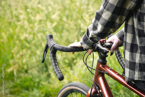 A man holds a bicycle handlebar and walks in the forest, close-up.