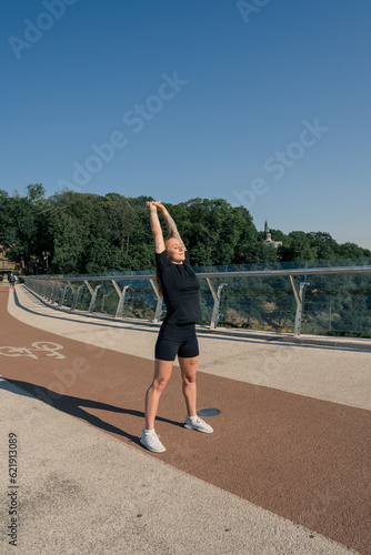 Fitness young sportswoman girl in the morning doing warm-up exercises before training on the street in the city on the bridge Sport health