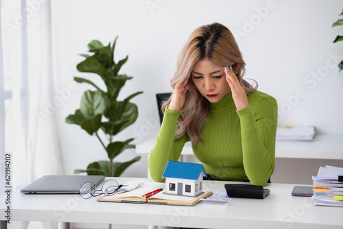 oung Asian woman sitting and calculating expenses and mortgage with calculator and house on table Worried about payments and non-repayable loans, business, and property