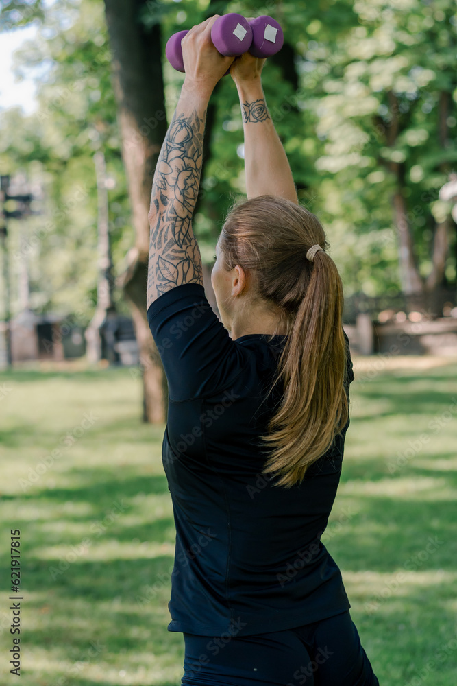 portrait of a young satisfied sports girl doing exercises with dumbbells outdoors during a workout in the park healthy lifestyle concept