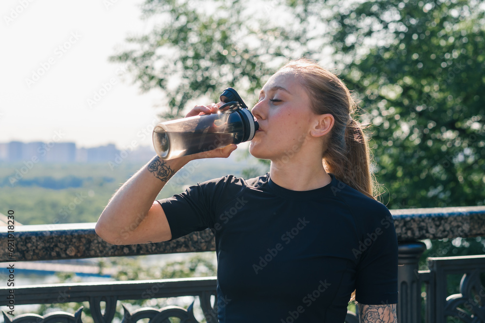 Fitness young sportswoman girl with tattoos doing sports in the morning drinking water while exercising outdoors in the city in the park health