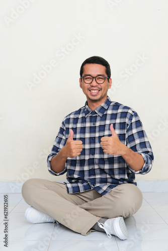 A man sitting cross legged on the floor smiling and give two thumbs up photo