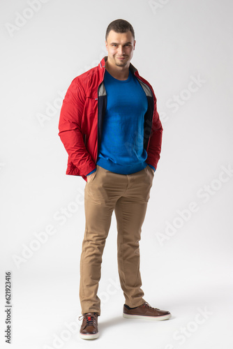 A man of athletic build in a red jacket stands and holds his hands in his pockets
