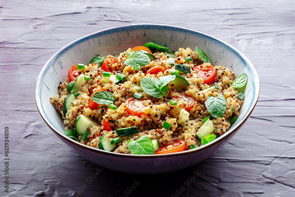 Quinoa tabbouleh salad in a bowl, a healthy dinner with tomatoes and mint on a purple background