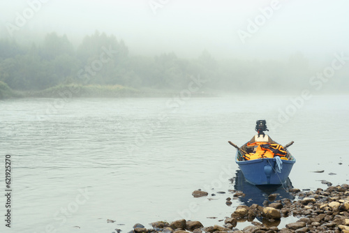 Fishing blue motorboat on a rocky river bank in the early morning in a foggy haze. High quality photo © Marina