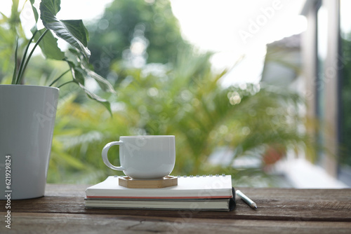 white coffee cup and books and pencils and pothos plant pot on brown wooden table