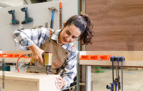 Portrait Young Latin woman carpenter using nailer shooting on wood. to restore furniture in the carpentry workshop photo