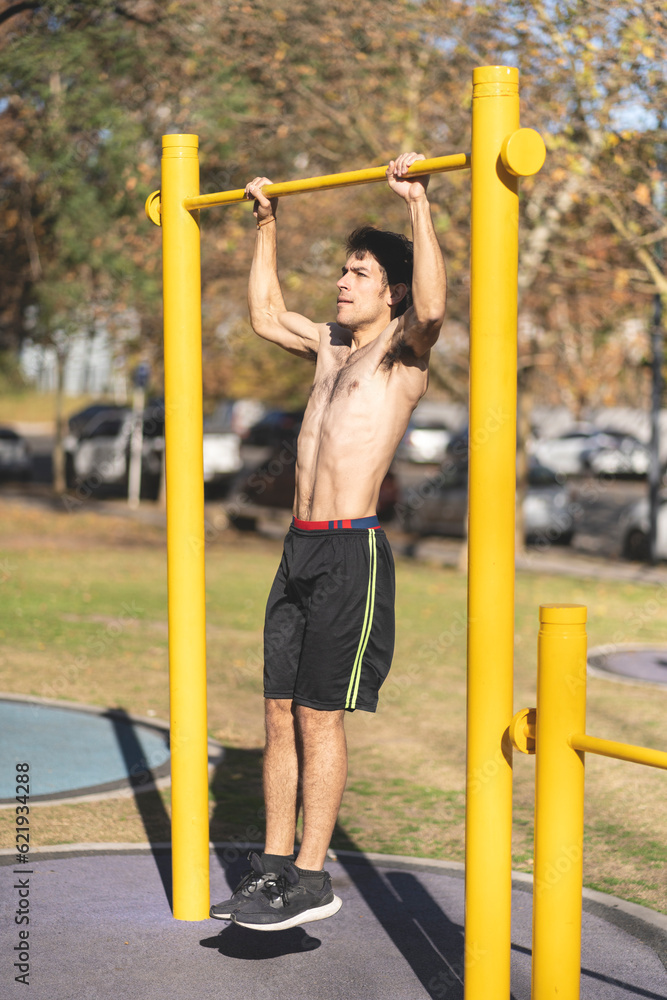 Obraz premium Young man doing pull ups on a crossbar at a park
