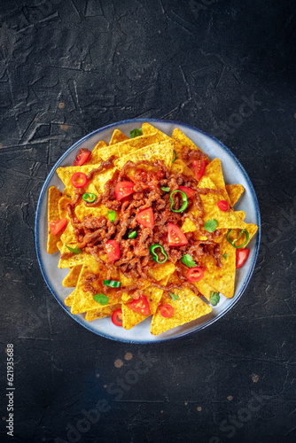 Nachos, Mexican food, tortilla chips with beef and fresh vegetables, overhead shot on a black background