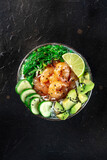 Shrimp poke bowl with avocado, cucumbers, wakame, and lime, shot from the top on a black background