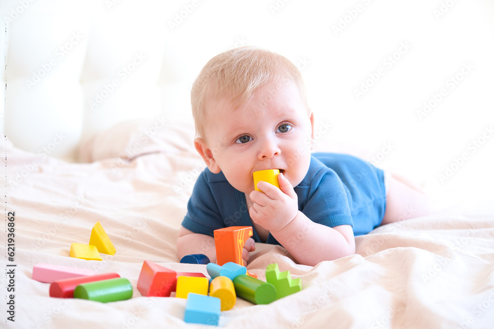 baby boy in blue bodysuit playing with colorful wooden eco toys on bed baby boy in blue bodysuit playing with colorful wooden eco toys on bed