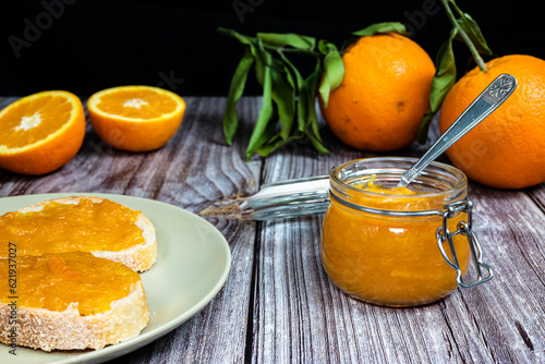 Delicious homemade orange marmalade in a glass jar. Jam on slice of bread on a plate. Horizontal photo with black background.