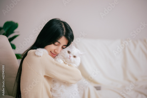 Young Asian beautiful woman increamy cardigan embracing her cat with love, relationship between pet and owner with warm and wellbeing of love concept.