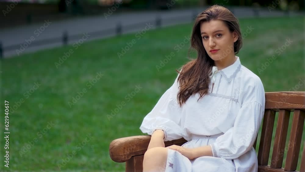 Portrait of thoughtful woman sitting on bench. Young female looking into camera on soft blurred background in park. Relax leisure activity, active lifestyle, cheerful confident attractive girl Portrait of thoughtful woman sitting on bench. Young female looking into camera on soft blurred background in park. Relax leisure activity, active lifestyle, cheerful confident attractive girl
