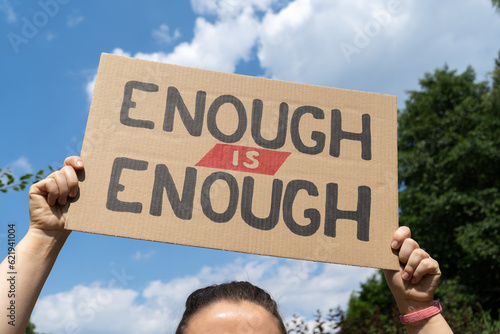 Woman holding placard sign with text Enough is enough. Female protestor with cardboard banner at protest rally demonstration. Call for change, demand action on the social justice matter.