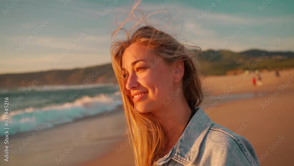 Woman smiling looking camera standing on ocean shore, wind blowing her hair. Portrait shooting happy blonde woman on beach. Young woman in denim shirt enjoying ocean views during sunset Woman smiling looking camera standing on ocean shore, wind blowing her hair. Portrait shooting happy blonde woman on beach. Young woman in denim shirt enjoying ocean views during sunset