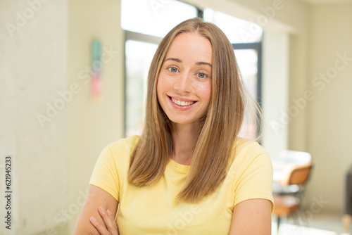 pretty blond woman smiling to camera with crossed arms and a happy, confident, satisfied expression, lateral view