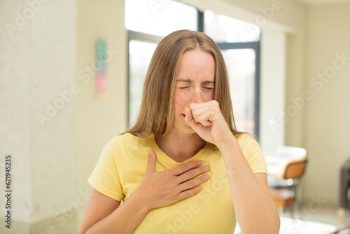 pretty blond woman feeling ill with a sore throat and flu symptoms, coughing with mouth covered