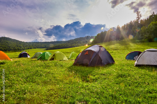 Tourists rest in a tent camp on a green field after a long passage. Tent city of pedestrian tourists in the summer in the mountains