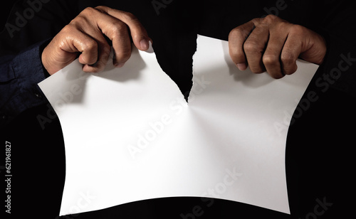 Male hand tearing paper close up on a dark background