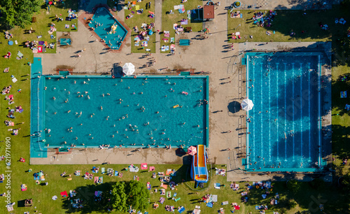 Obraz na płótnie Aerial view of a two large and crowded outdoor pool. People swim in blue water pool top view on a summer day. Pool in green park. w salonie