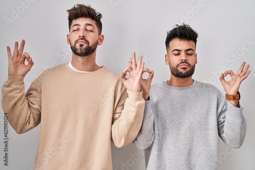 Young homosexual couple standing over white background relaxed and smiling with eyes closed doing meditation gesture with fingers. yoga concept.