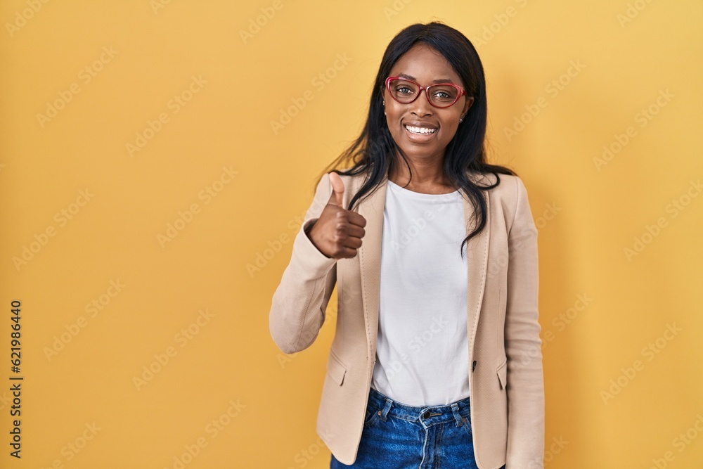 African young woman wearing glasses doing happy thumbs up gesture with hand. approving expression looking at the camera showing success. African young woman wearing glasses doing happy thumbs up gesture with hand. approving expression looking at the camera showing success.