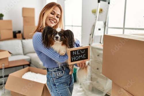 Young caucasian woman holding blackboard hugging dog at new home