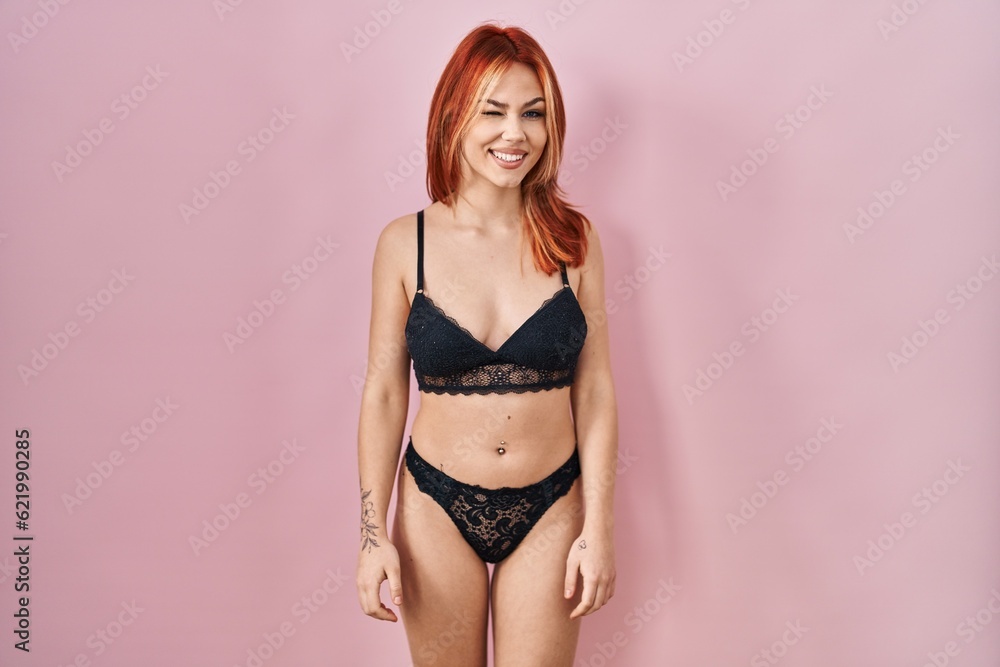 Young caucasian woman wearing lingerie over pink background winking looking at the camera with sexy expression, cheerful and happy face. Young caucasian woman wearing lingerie over pink background winking looking at the camera with sexy expression, cheerful and happy face.