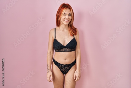 Young caucasian woman wearing lingerie over pink background winking looking at the camera with sexy expression  cheerful and happy face.