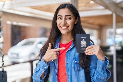 Young teenager girl holding canada passport smiling happy pointing with hand and finger