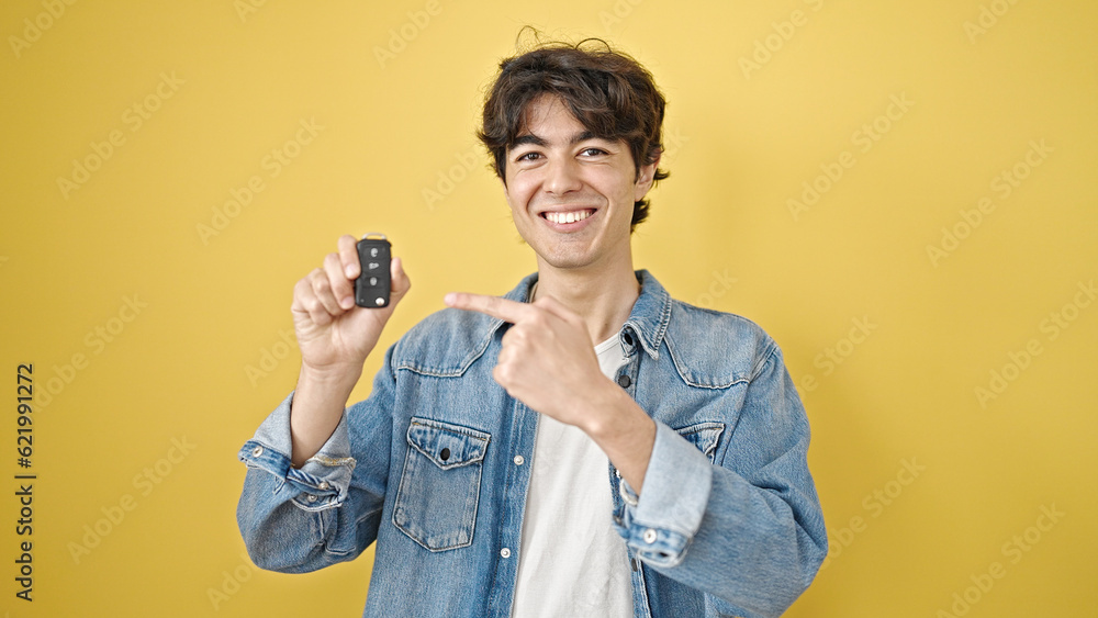 Young hispanic man smiling confident pointing to key of new car over isolated yellow background Young hispanic man smiling confident pointing to key of new car over isolated yellow background