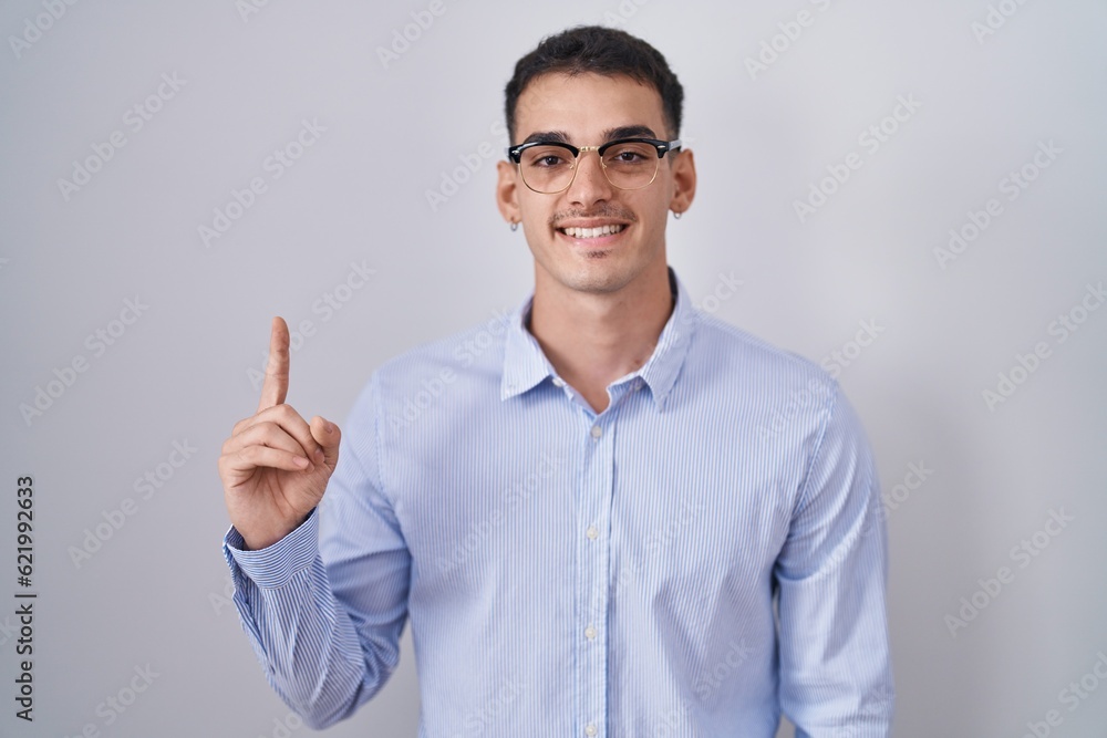 Handsome hispanic man wearing business clothes and glasses showing and pointing up with finger number one while smiling confident and happy. Handsome hispanic man wearing business clothes and glasses showing and pointing up with finger number one while smiling confident and happy.