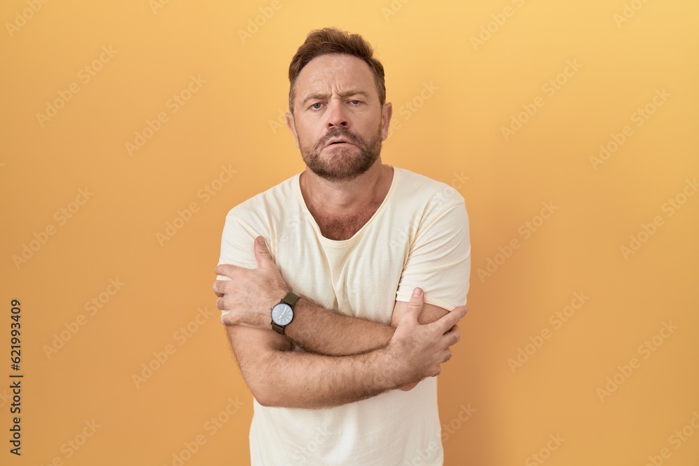Middle age man with beard standing over yellow background shaking and freezing for winter cold with sad and shock expression on face Middle age man with beard standing over yellow background shaking and freezing for winter cold with sad and shock expression on face