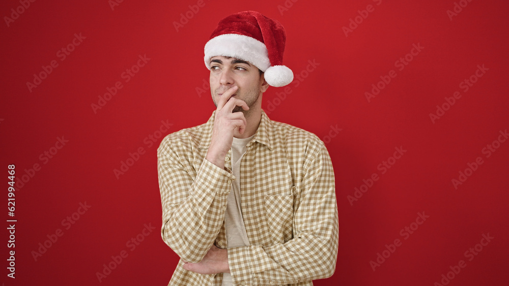 Young hispanic man wearing christmas hat with doubt expression over isolated red background Young hispanic man wearing christmas hat with doubt expression over isolated red background