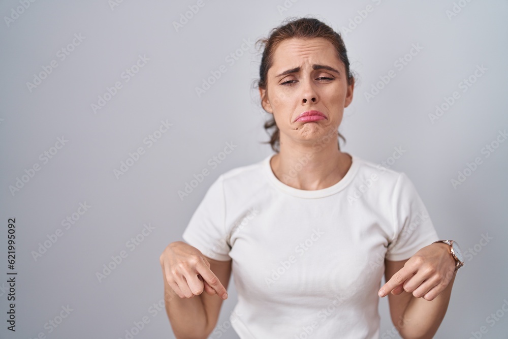 Beautiful brunette woman standing over isolated background pointing down looking sad and upset, indicating direction with fingers, unhappy and depressed. Beautiful brunette woman standing over isolated background pointing down looking sad and upset, indicating direction with fingers, unhappy and depressed.