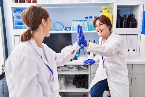 Two women scientist smiling confident high five with hands raised up at laboratory