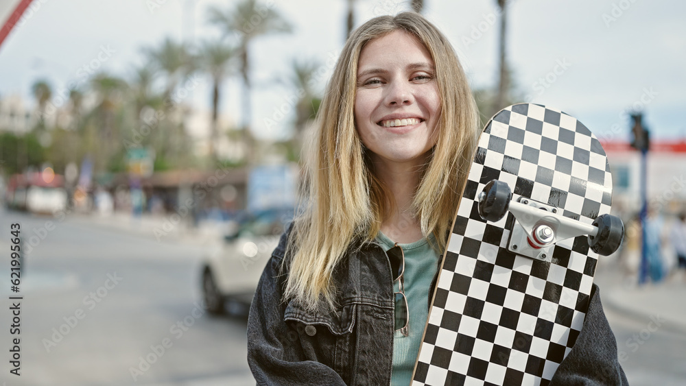 Fototapeta premium Young blonde woman smiling confident holding skate at street