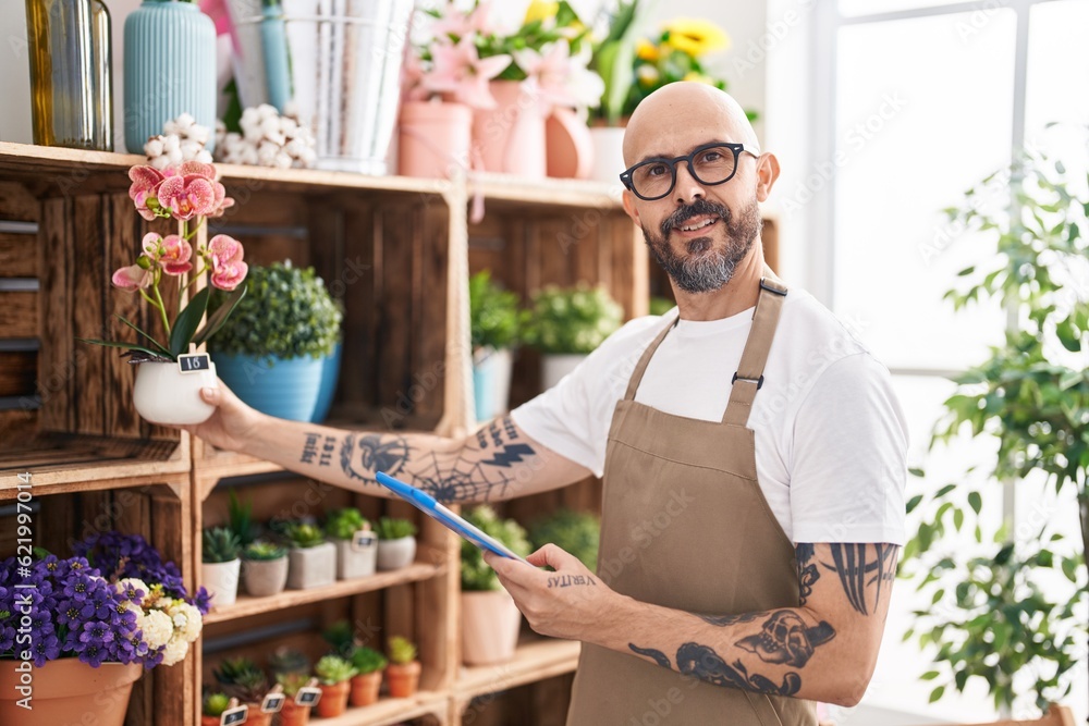 Young bald man florist using touchpad holding plant at florist Young bald man florist using touchpad holding plant at florist